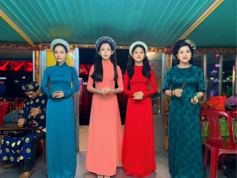 Nghệ sĩ biểu diễn nhã nhạc cung đình trên thuyền rồng trên sông Hương buổi tối, tạo không khí trang trọng, truyền thống.